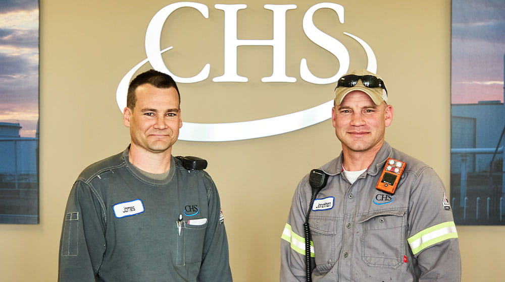 Two men standing beside CHS logo